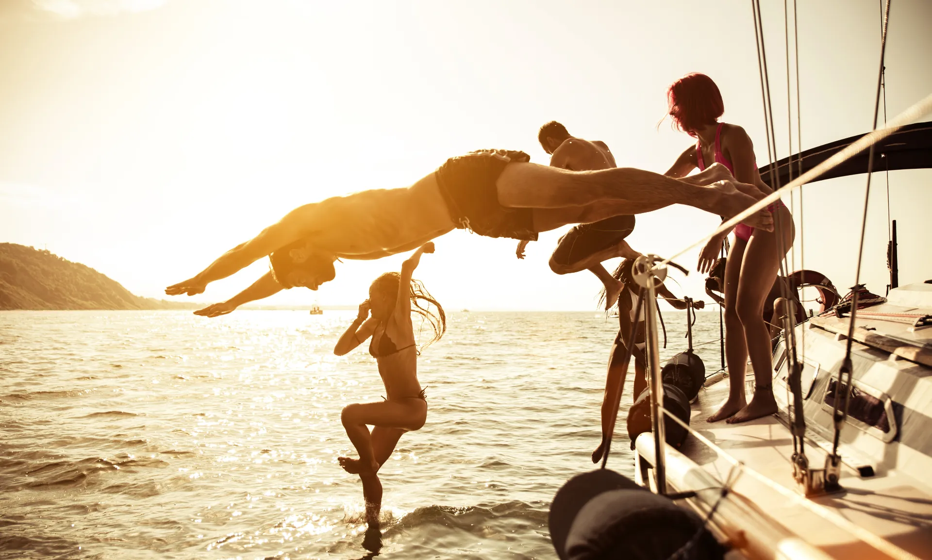 Freunde springen bei Sonnenuntergang vom Segelboot ins Meer